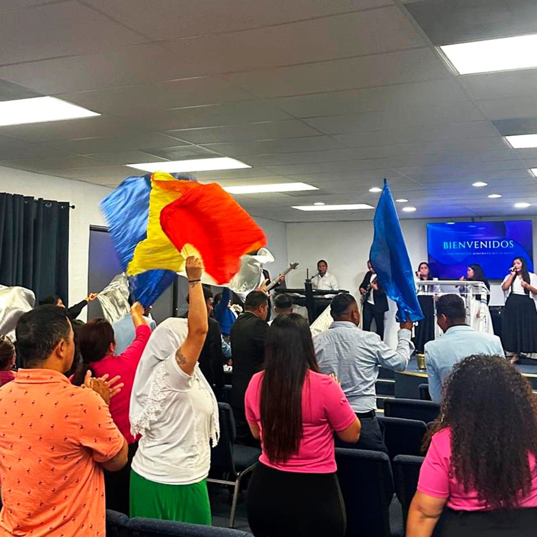 Congregación de pie adorando con banderas de colores durante el servicio